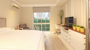 A modern hotel room with a large bed, a desk with a computer, a chair, a TV, and a window with a city view. - Havenwood Residence TB Simatupang (Jakarta)