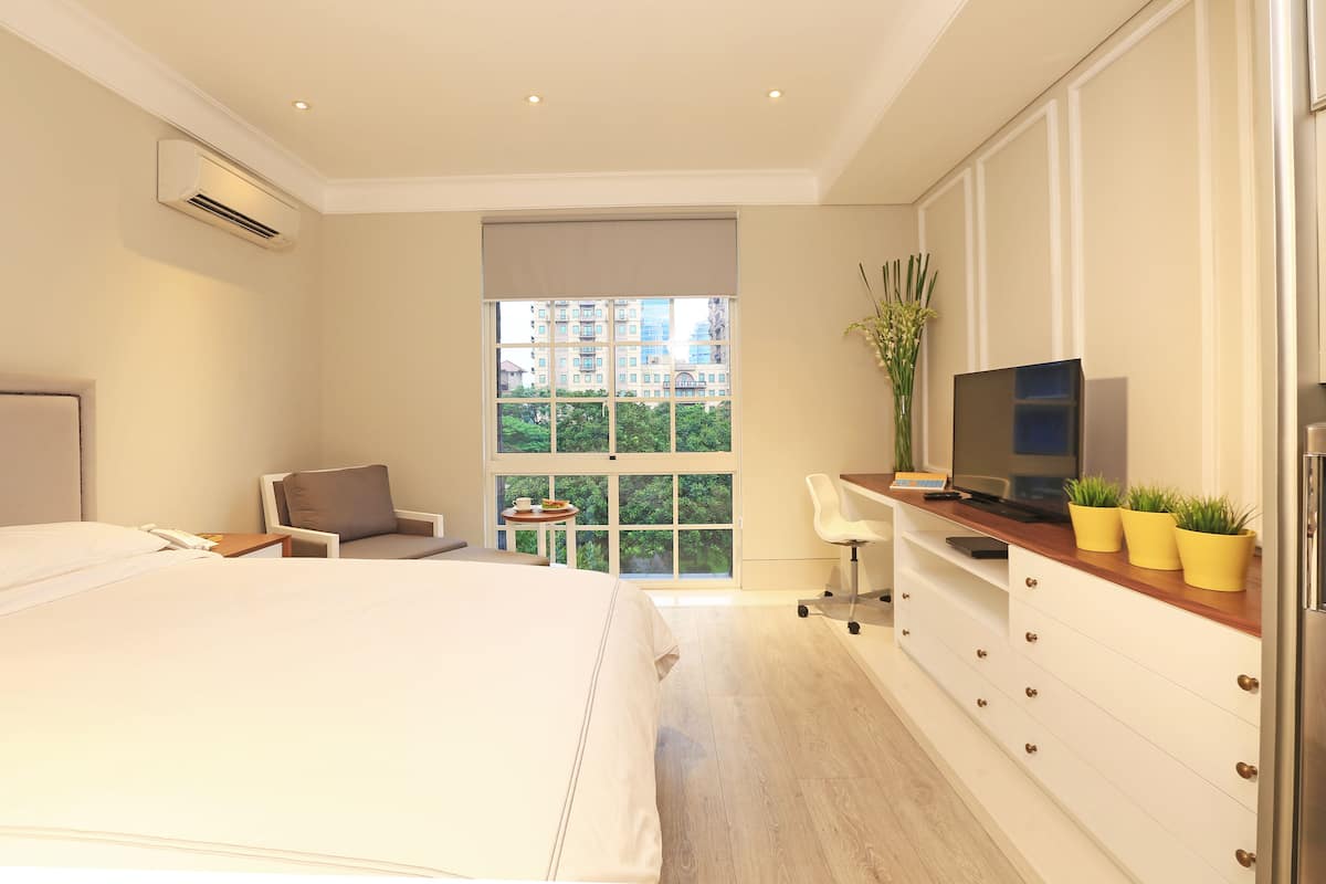 A modern hotel room with a large bed, a desk with a computer, a chair, a TV, and a window with a city view.