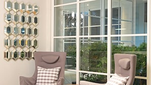 A modern room with two grey armchairs, a hexagonal mirror wall, and large windows offering a view of greenery. - Havenwood Residence TB Simatupang (Jakarta)