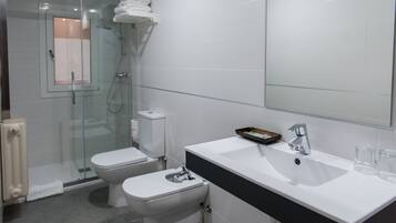 Uma casa de banho moderna com cabine de chuveiro em vidro, sanita branca e lavatório branco com bancada preta.