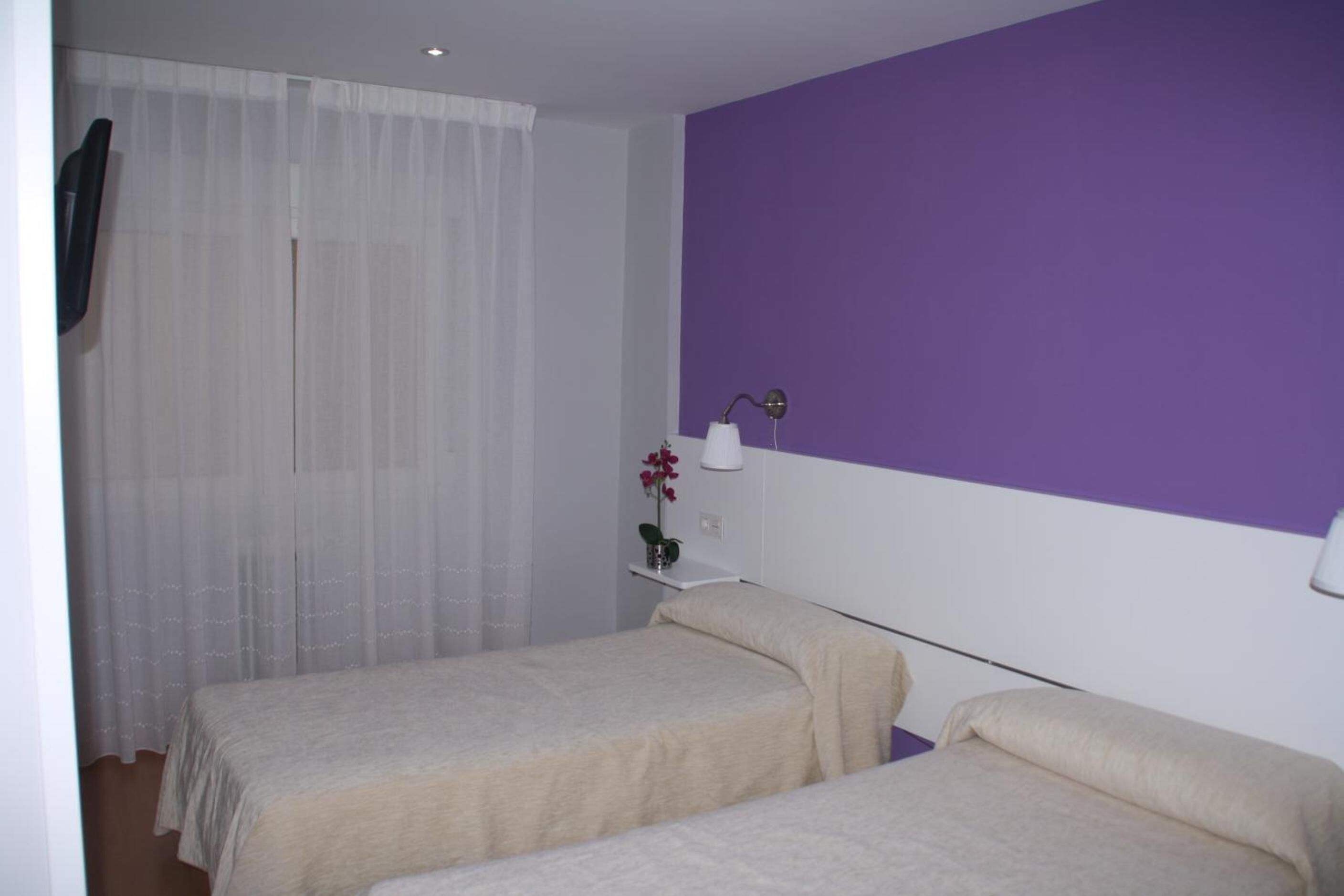 A room with two beds, a white wall, and a purple accent wall.