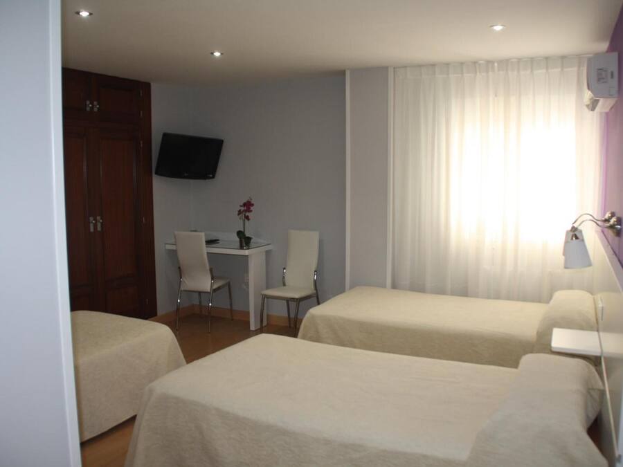 Una habitación de hotel con dos camas, un escritorio, una silla, un televisor y una ventana con cortinas.