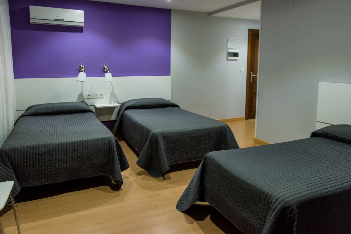 Habitación de hotel con dos camas individuales, una mesita de noche, una lámpara y aire acondicionado instalado en la pared.