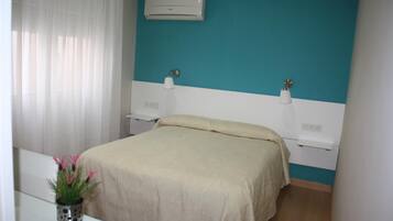 Un dormitorio con cama, mesitas de noche, aire acondicionado y una ventana con cortinas.