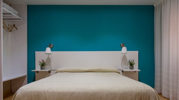 Une chambre avec un mur d’accent de couleur turquoise, une tête de lit blanche, deux tables de chevet avec des lampes et un lit recouvert d’une couvre-lit beige.