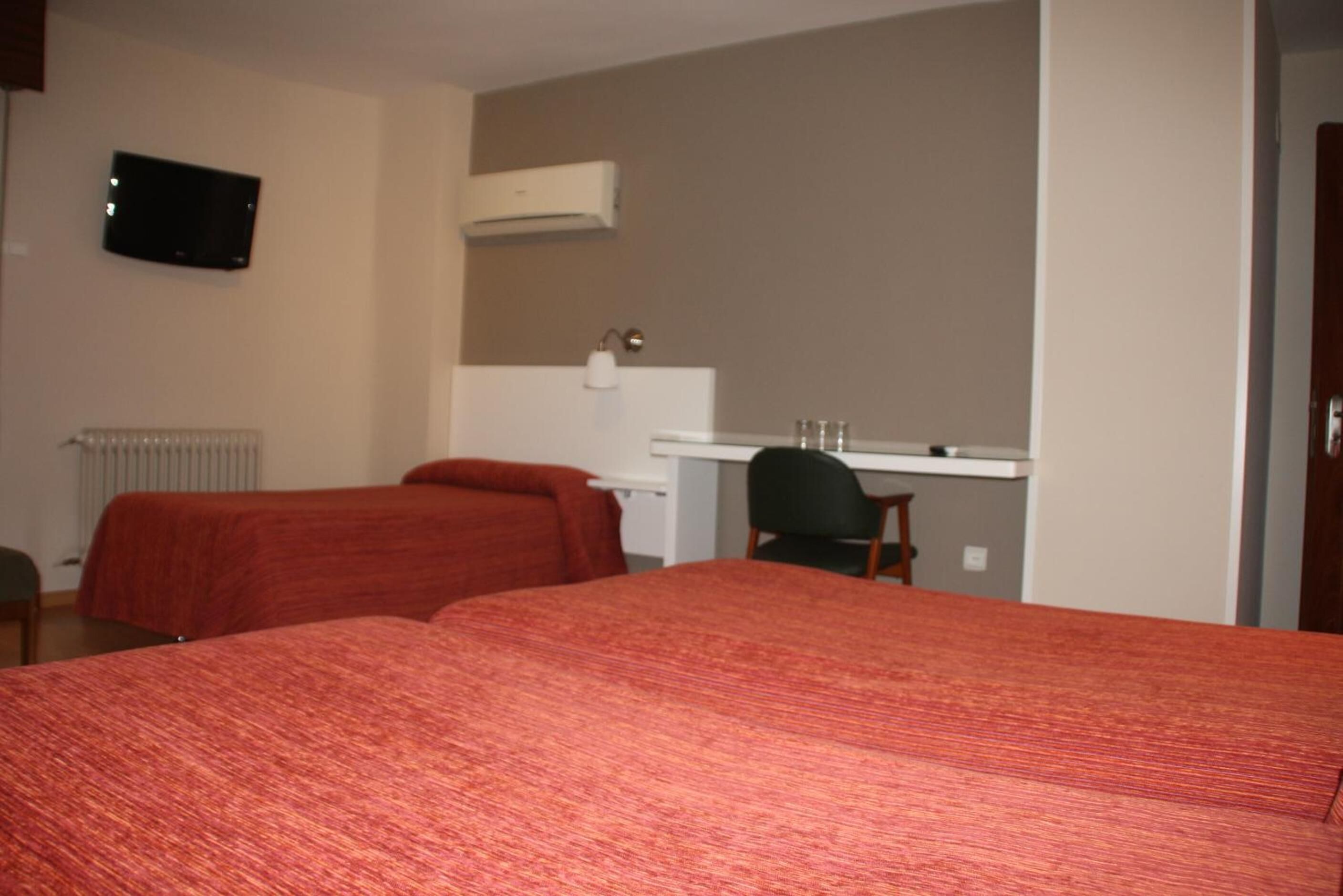 Habitación de hotel con dos camas, un escritorio, una silla, un televisor y un equipo de aire acondicionado.
