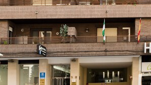 Un immeuble à plusieurs étages, avec une entrée au niveau du sol, des balcons ornés de plantes et des drapeaux.