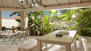 Eine Terrasse im Freien mit einem weißen Tisch und Stühlen, umgeben von üppiger Bepflanzung und Steinmauern.