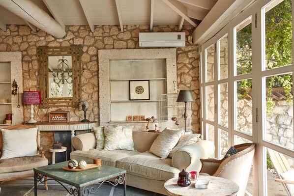 A cozy room with a stone wall, a fireplace, a sofa, a table, and a large window.