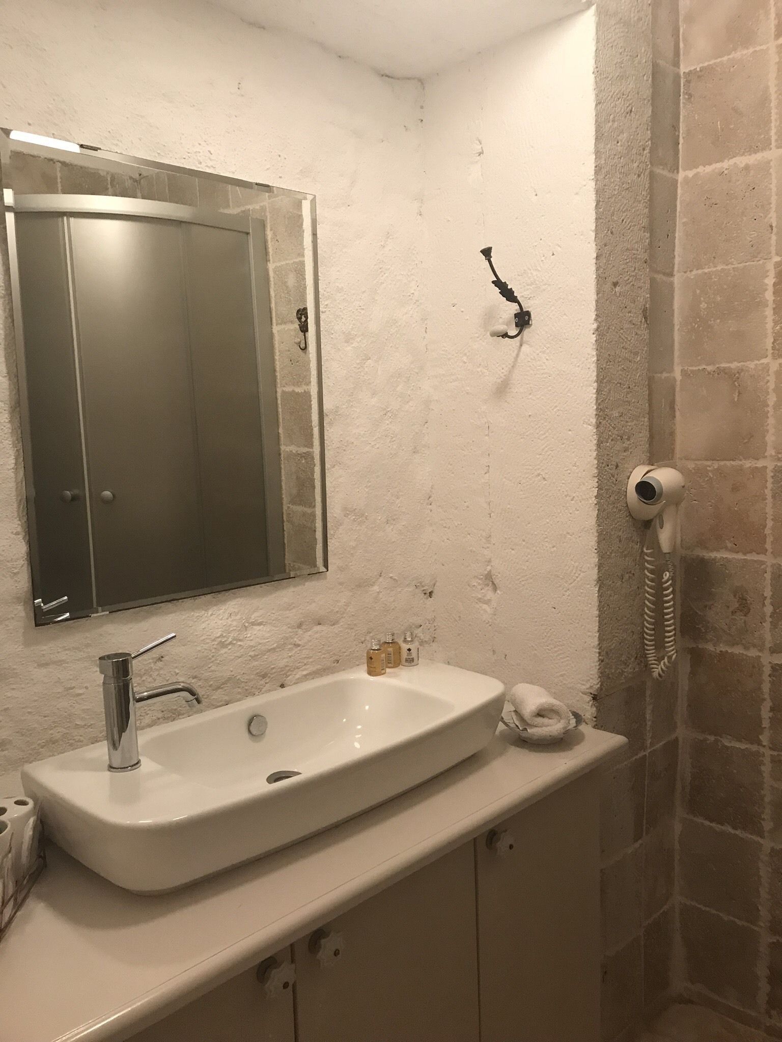 Une salle de bain avec un lavabo blanc, un miroir, un porte-serviettes et une douche équipée d’un pommeau de douche à main.