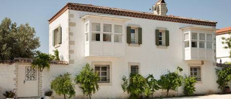 A white building with a tiled roof, multiple windows with shutters, and a small balcony.
