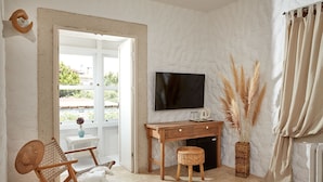 Ein gemütliches Zimmer mit einem Holztisch, einem Fernseher, einem Korbstuhl und Blick ins Grüne.