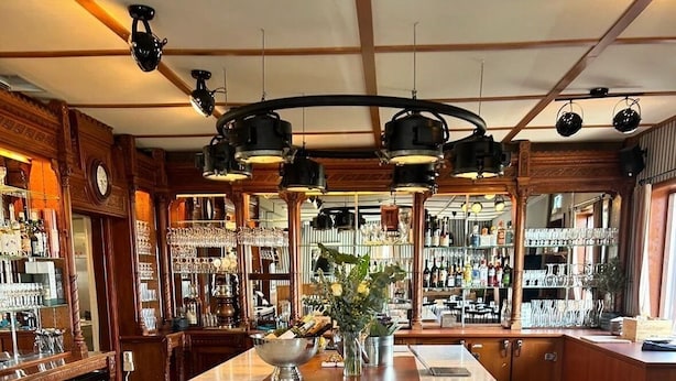 Zona de bar con piso a cuadros, taburetes de madera y una isla central con un jarrón de flores.