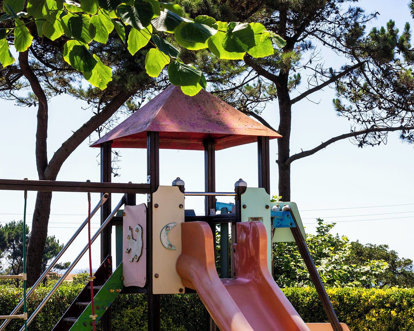 A playground structure with a slide, climbing net, and a shelter.