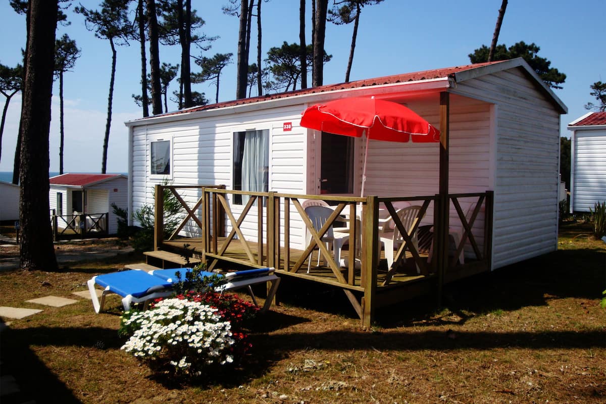 A small, single-story cabin with a red roof and a wooden deck.