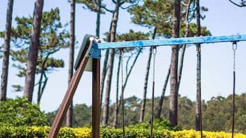 A swing set in a park with tall trees and trimmed bushes in the background.