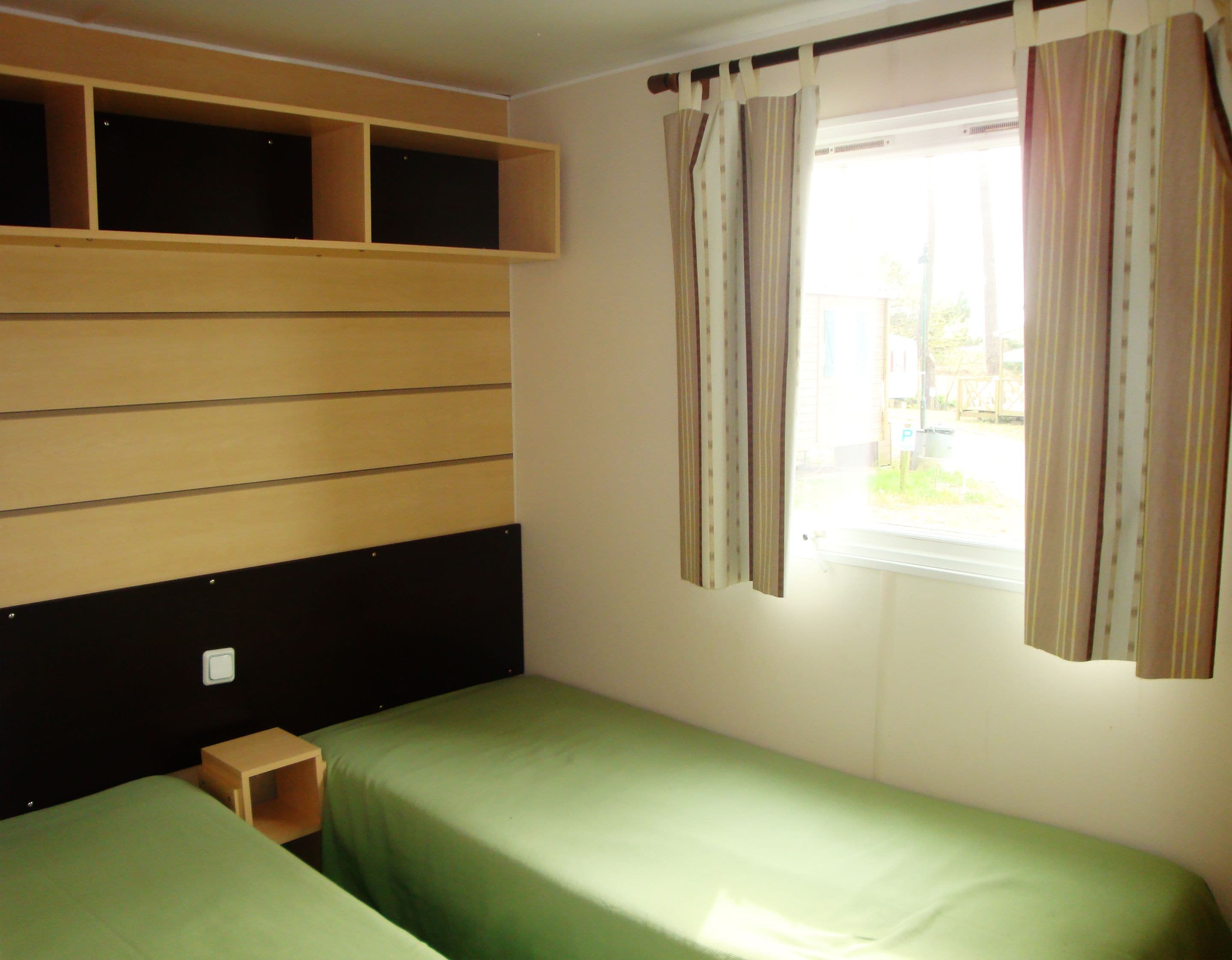 Habitación individual con una cama y cabecera de madera, una mesita de noche de madera y una ventana con cortinas.