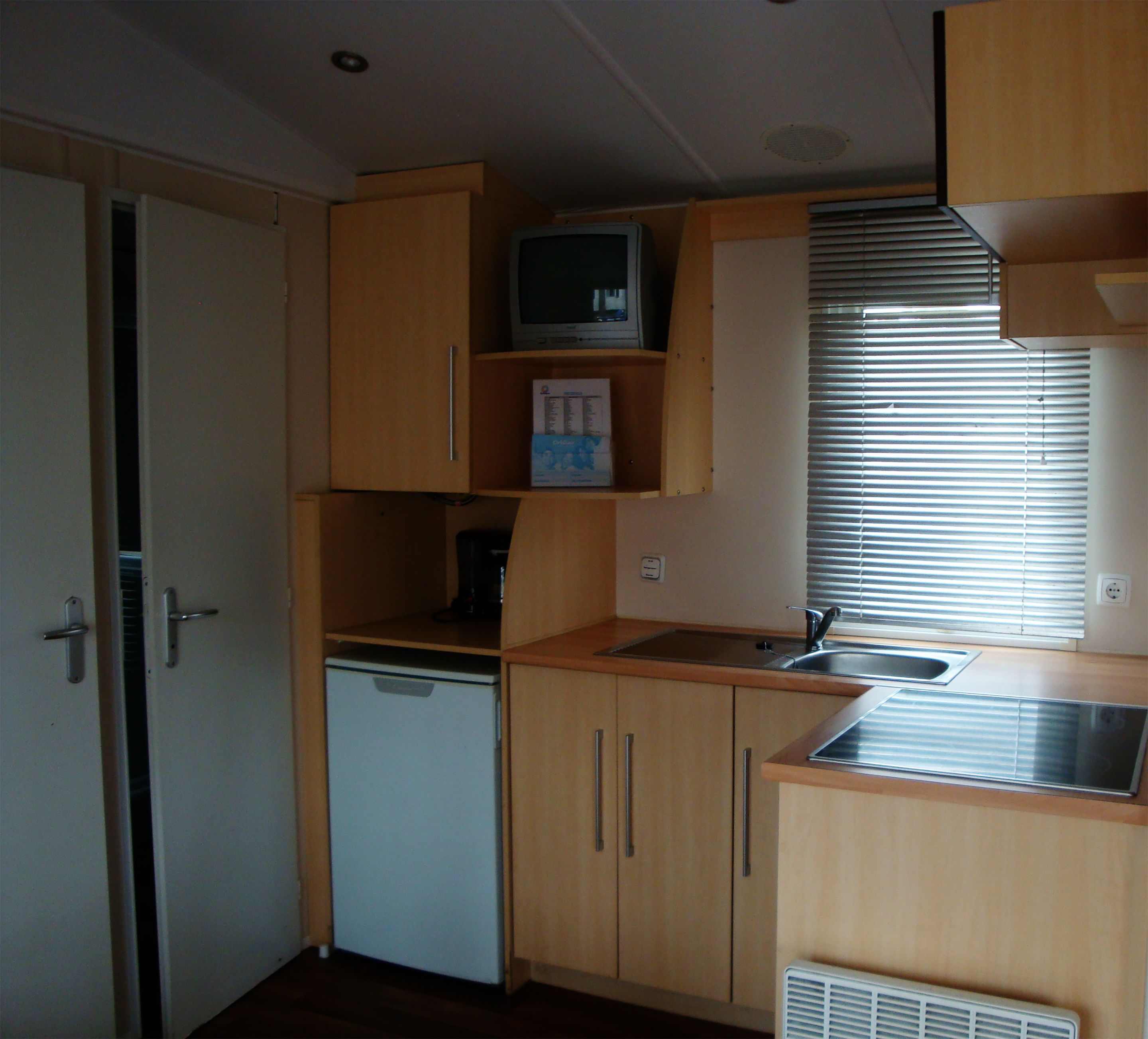 A compact kitchenette with wooden cabinets, a small refrigerator, a microwave, and a sink.