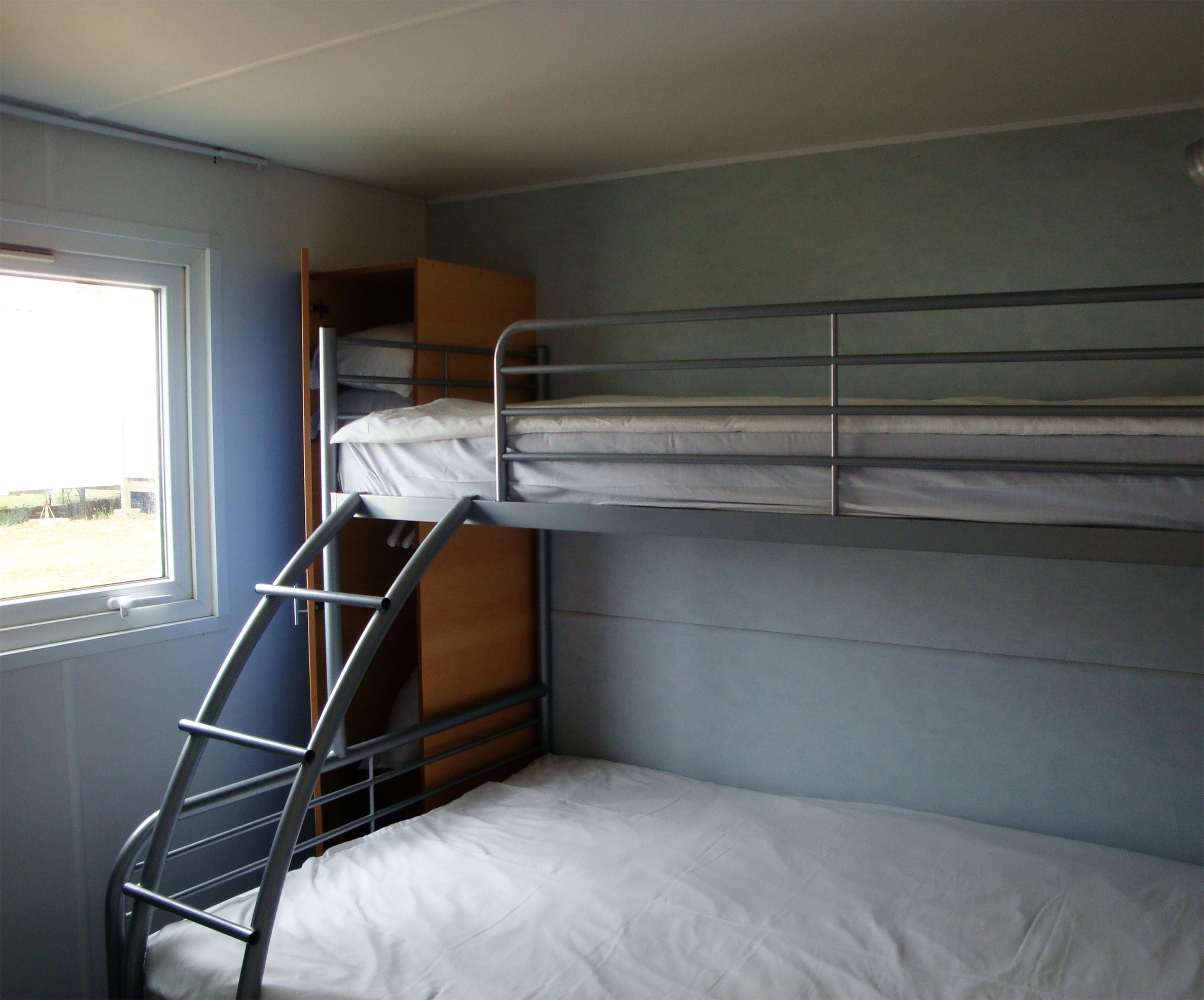 A bunk bed with a ladder, a window, and a wooden cabinet.