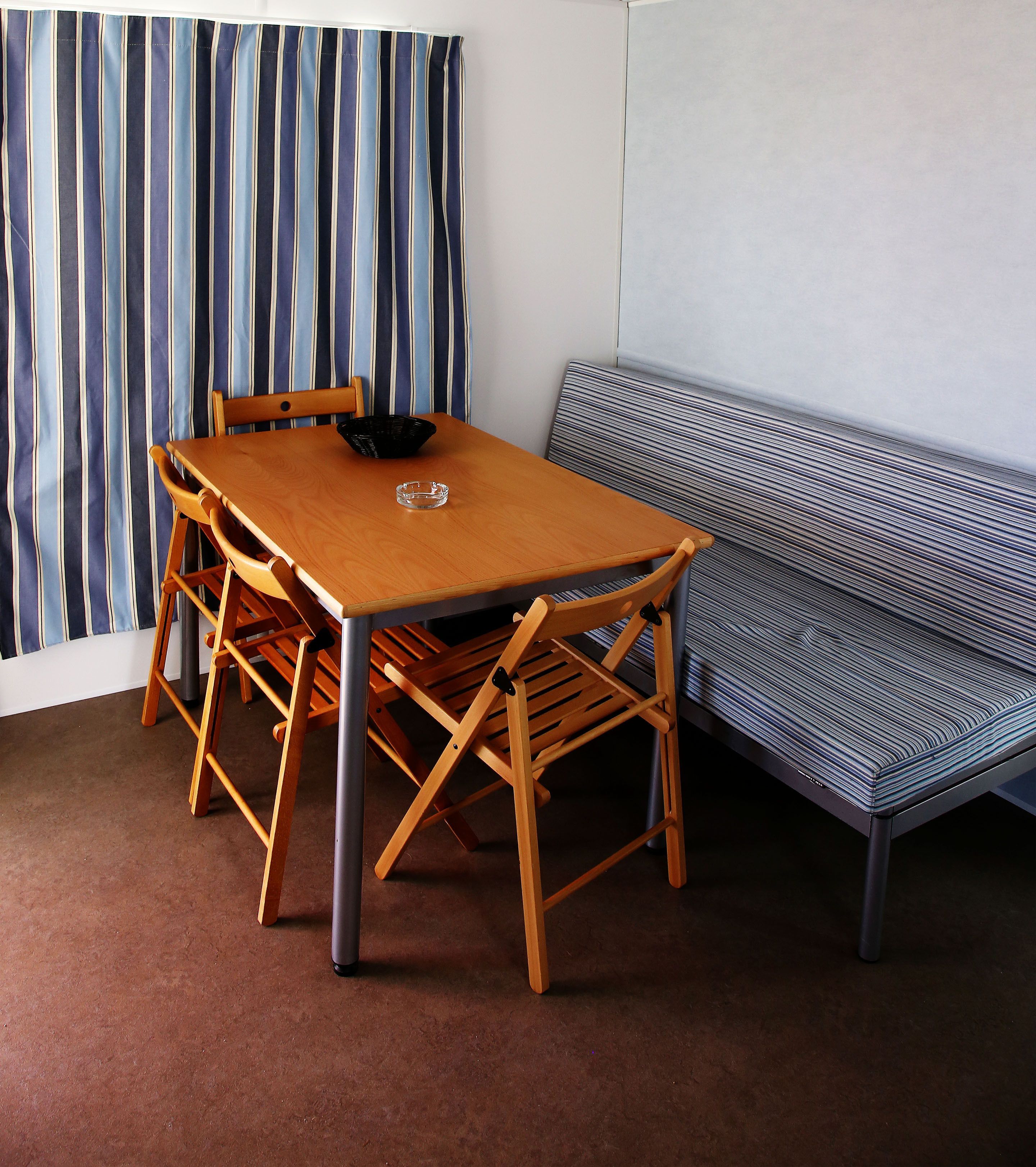 A dining area with a wooden table and chairs, a bench, and a striped curtain.