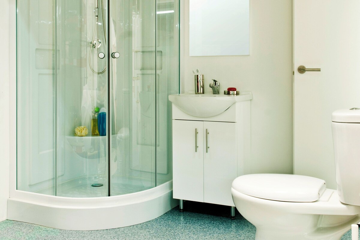 A bathroom with a glass-enclosed shower, a sink with a mirror above it, and a toilet.
