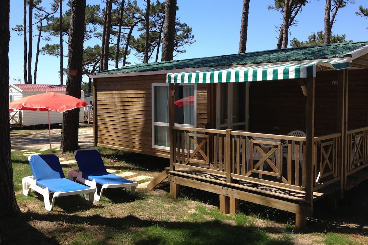 A wooden cabin with a deck, two lounge chairs, and a red umbrella.
