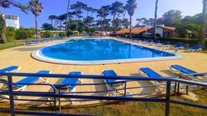 Una piscina con sillas reclinables azules y una zona de cubierta arenosa.