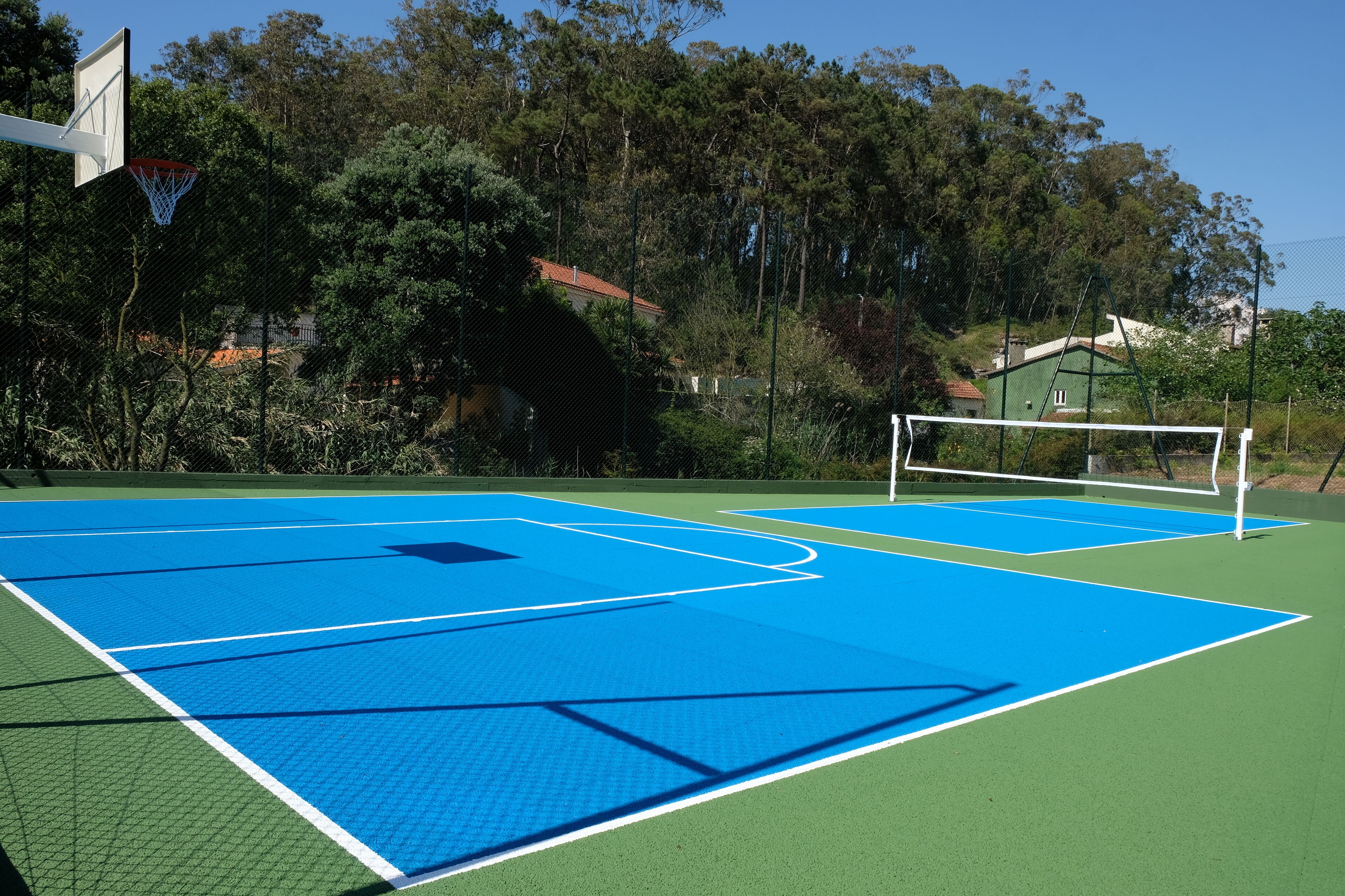 An outdoor basketball court with a net, surrounded by trees and houses.