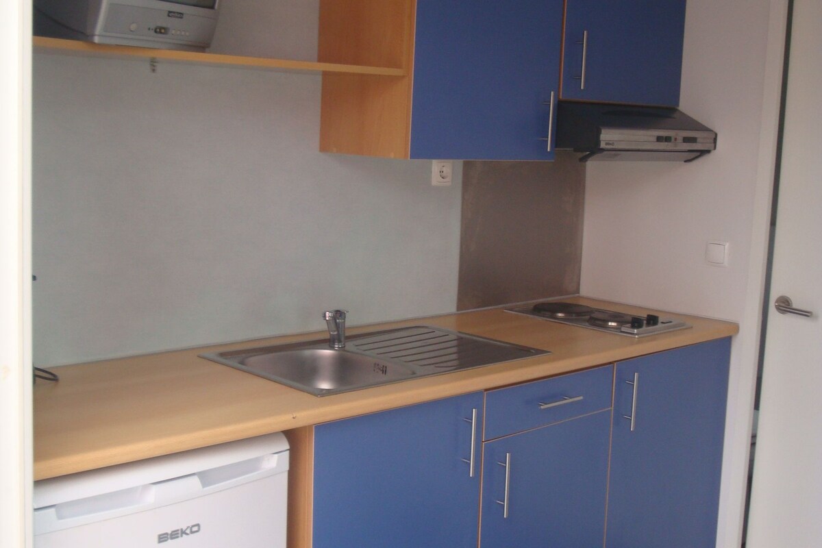 Una cocina compacta con un lavamanos, un refrigerador pequeño y armarios azules.