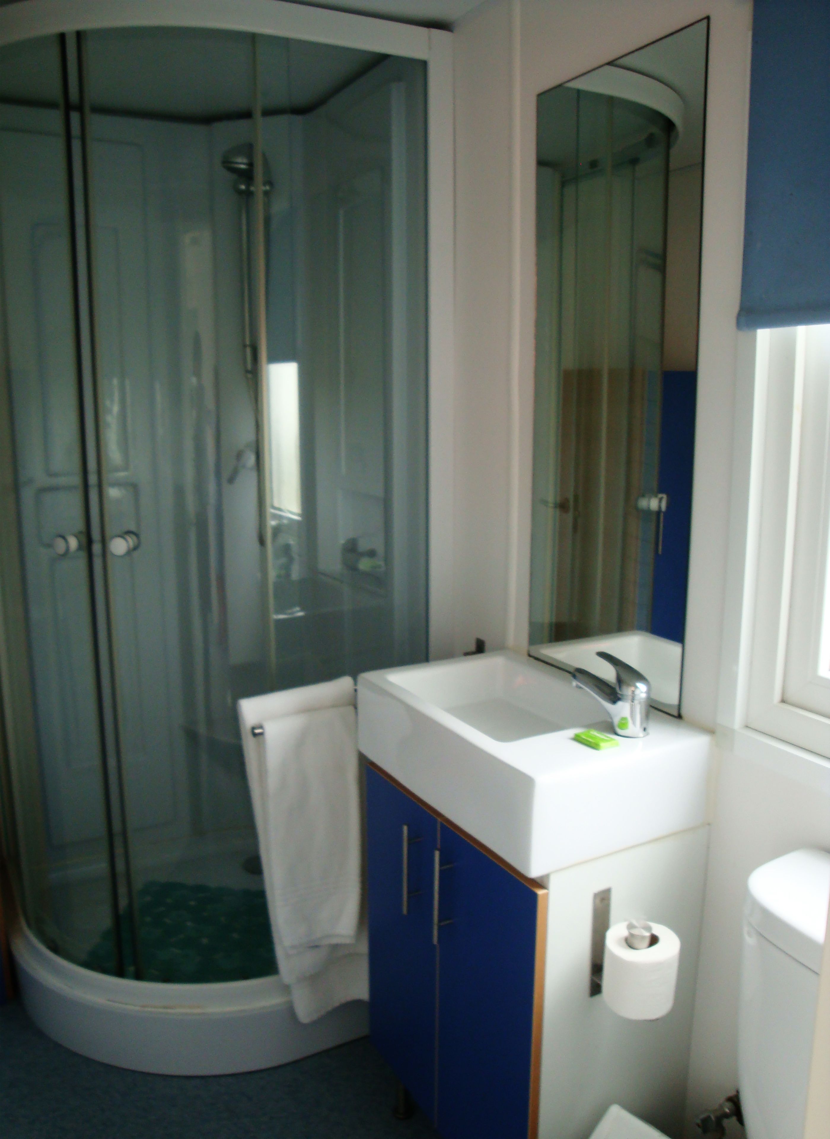 Une salle de bain avec une douche à parois de verre, un lavabo blanc avec un miroir et un meuble bleu.