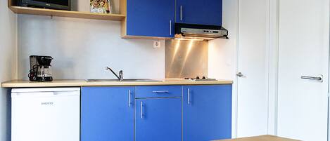 Una cocina compacta con armarios azules, un refrigerador blanco, un microondas y una cafetera.