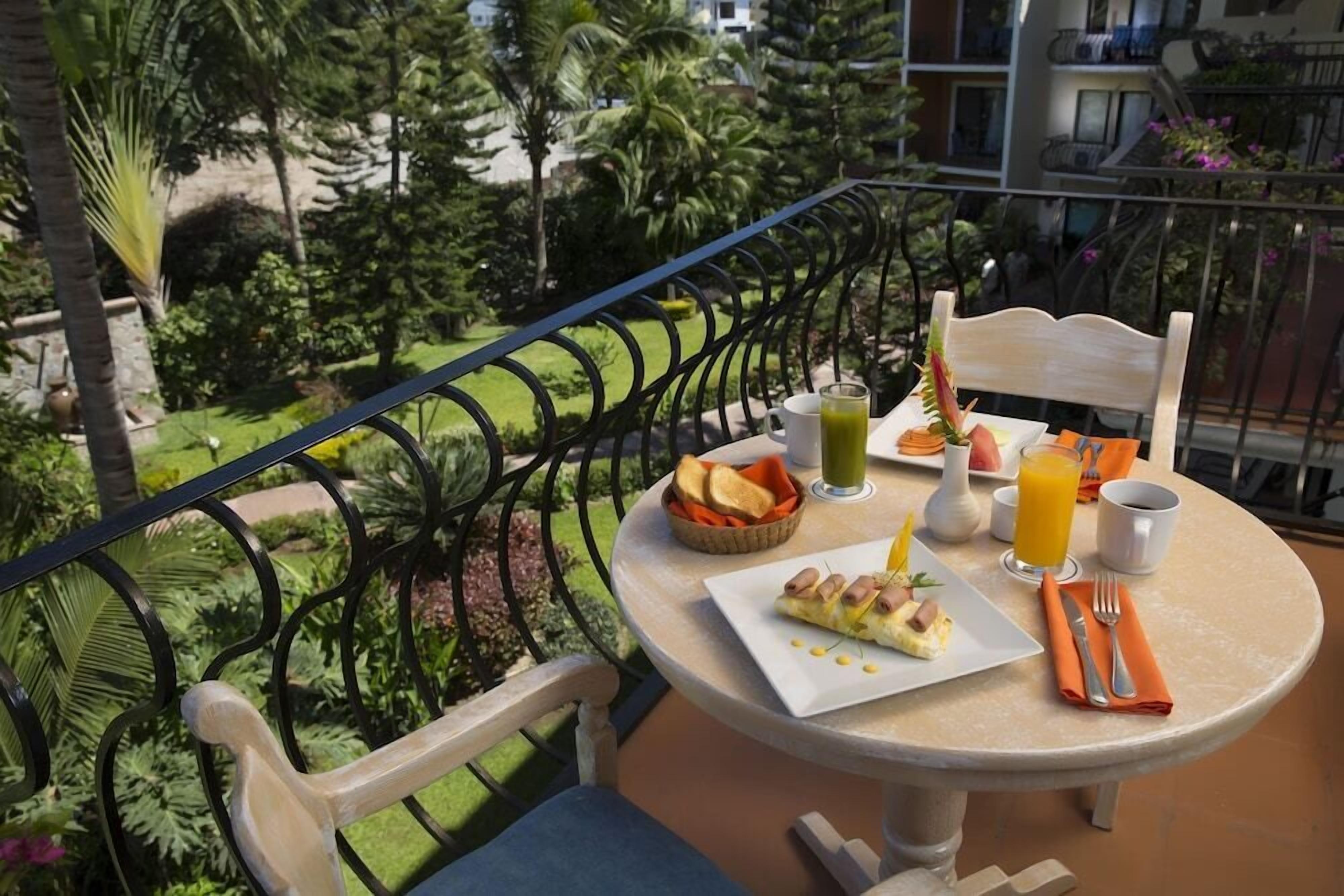 Uma varanda com uma mesa posta para o café da manhã, incluindo torradas, frutas e um prato de ovos.