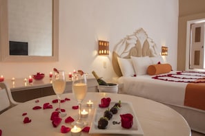 A hotel room with a bed, a bedside table with candles, a bottle of champagne, and rose petals on the table. - The Hotel Flamingo Vallarta (PUERTO VALLARTA)