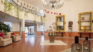 Eine geräumige Lobby mit hoher Decke, einer Chandelierleuchtre, einer Treppe mit Geländer und einer Sitzecke mit Tisch und Stühlen.