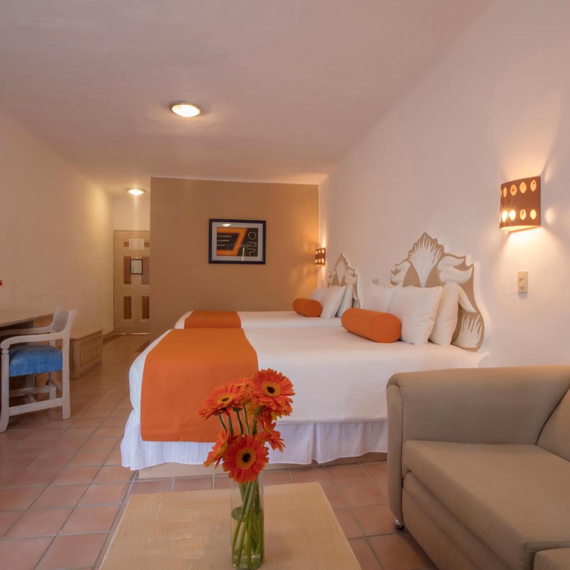 Una habitación de hotel con cama, escritorio, silla, sofá y un florero con flores.