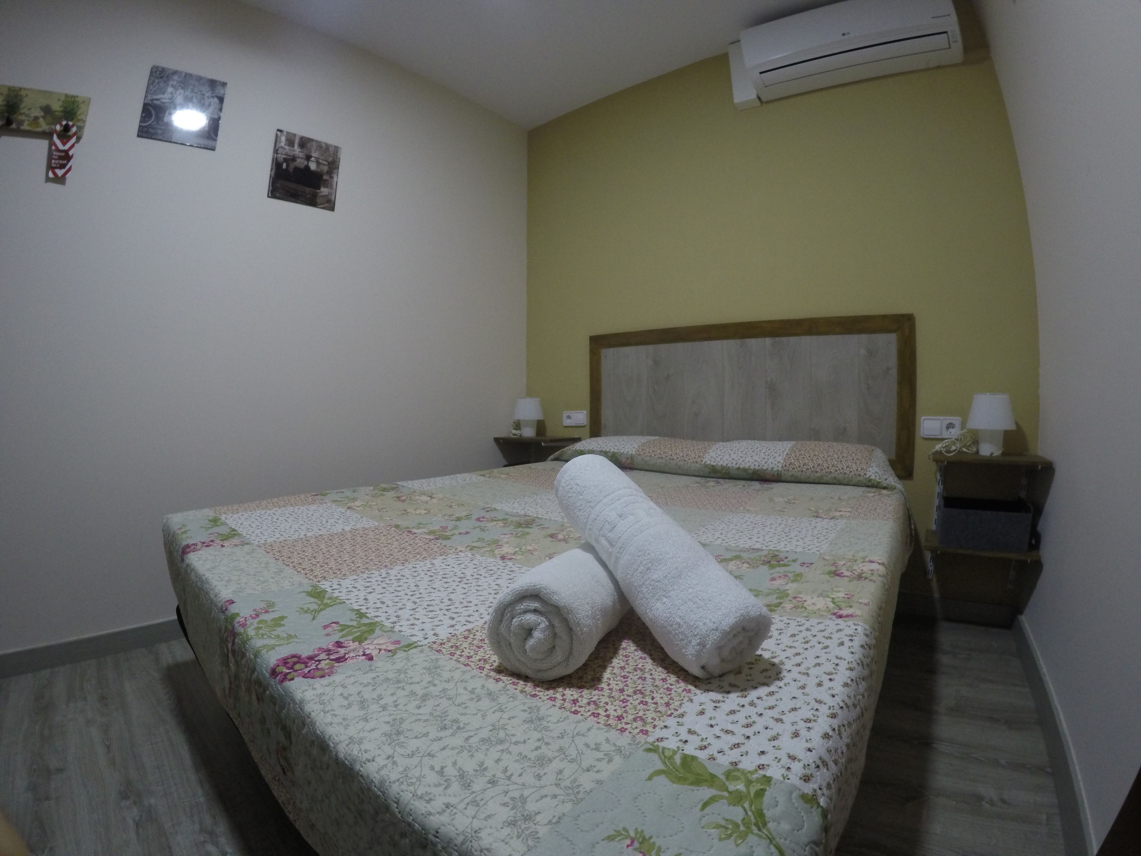 A hotel room with a bed, two bedside tables, an air conditioner, and a wall-mounted picture.