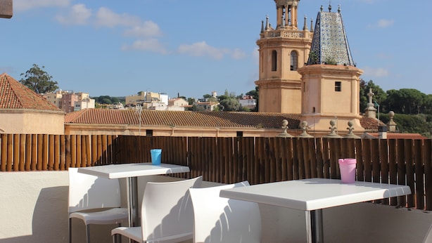 Une terrasse avec des tables et des chaises blanches, une clôture en bois et une vue sur un bâtiment historique doté d’une tour.