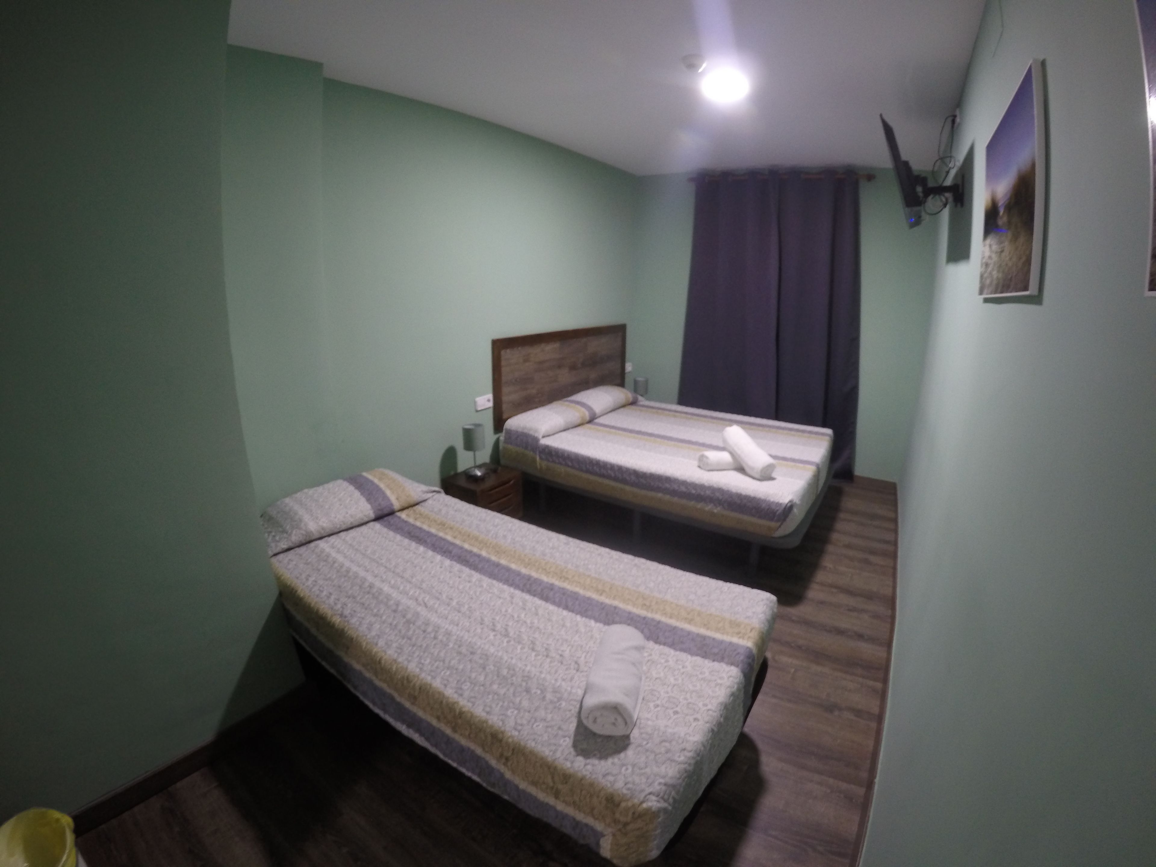 Une petite pièce simple, avec deux lits, une table de chevet, une lampe et un tableau au mur.