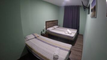 Una habitación pequeña y sencilla con dos camas, una mesita de noche, una lámpara y un cuadro en la pared.