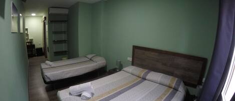 Quarto de hotel com duas camas, cabeceira de madeira e uma pequena mesa com cadeira.