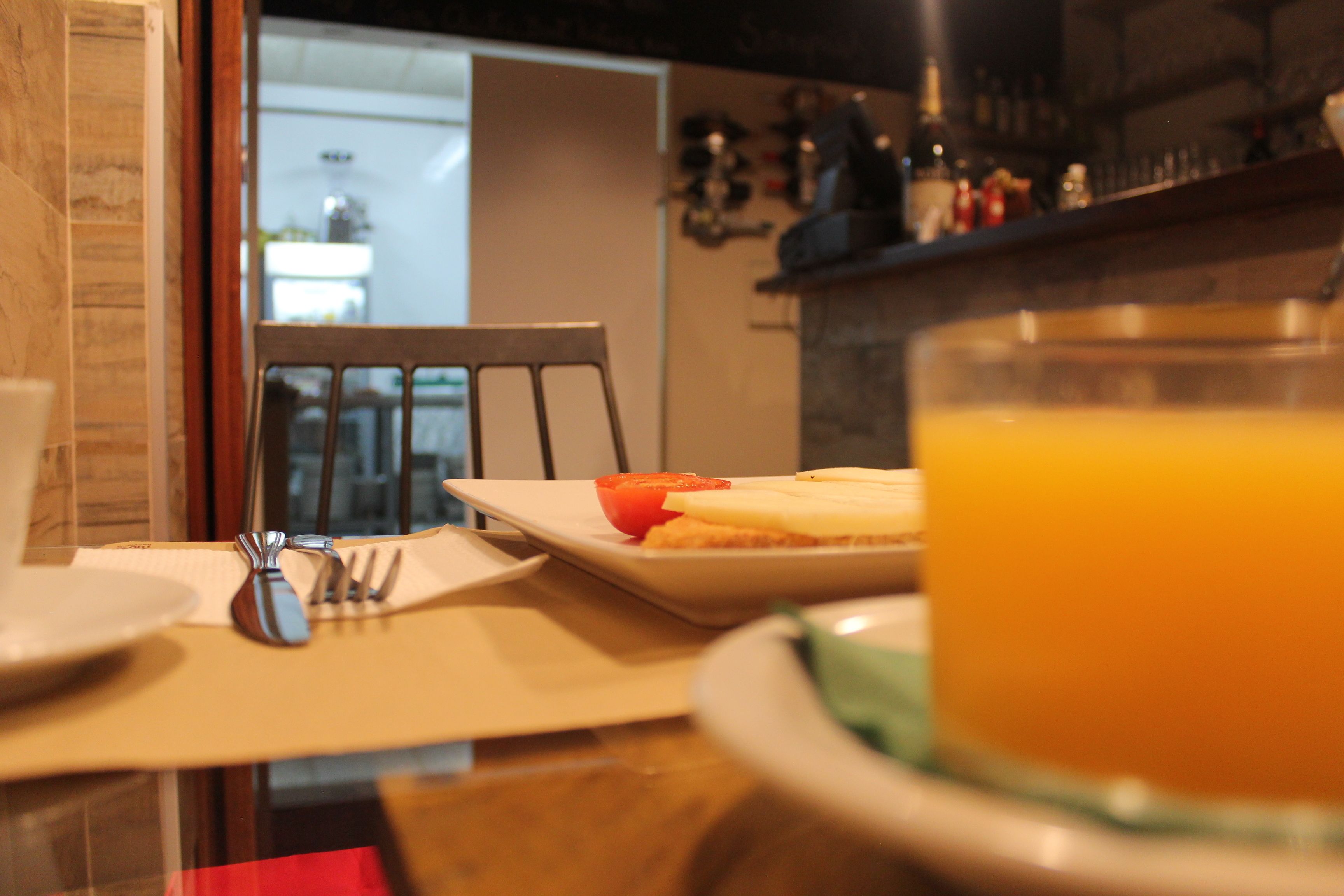 Mesa de café da manhã com um prato de comida, um copo de suco de laranja e talheres.