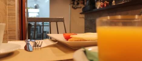 Mesa de café da manhã com um prato de comida, um copo de suco de laranja e talheres.