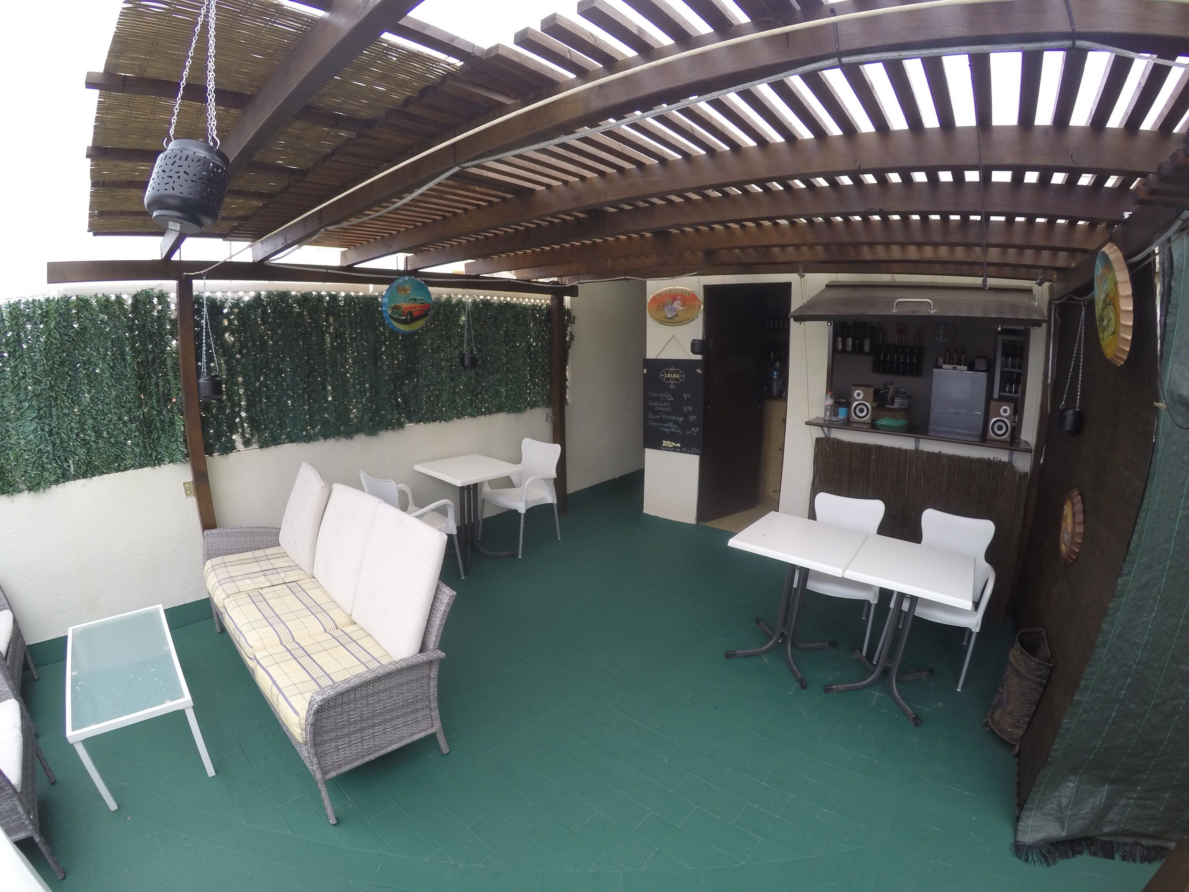 Un patio al aire libre con un área de estar techada, un bar y una pared verde.