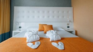 A hotel room with a large bed, white headboard, orange bedding, and a nightstand with a lamp. - Hotel Viest (Vicenza)