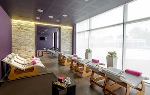 A spa room with multiple massage tables, a stone wall, and large windows. - Hotel Viest (Vicenza)