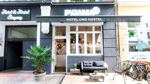 A hotel and hostel exterior with a sign reading "PIJAMA HOTEL UND HOSTEL," a wooden bench, a chair, and a potted plant. - Pyjama Park Schanzenviertel - Hostel (Hamburg)