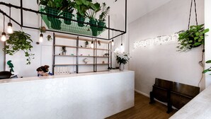 A reception area with a white hexagonal tile floor, wooden shelves with plants, a green hanging plant, and a neon sign. - Pyjama Park Schanzenviertel - Hostel (Hamburg)