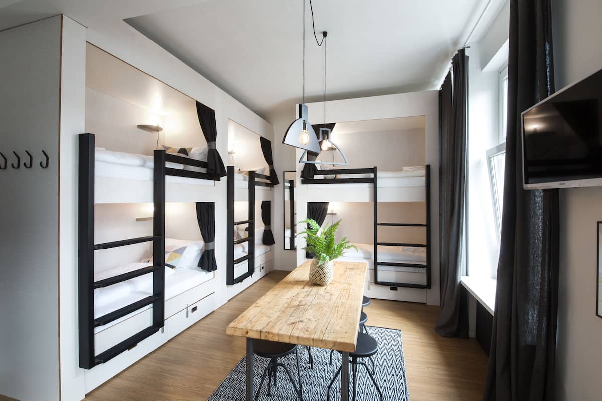 A modern, compact room with bunk beds, a wooden dining table, and a TV.