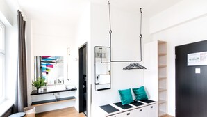 A modern hotel room with a wooden floor, a black and white bench with teal cushions, a black door, and a white wall with a mirror and shelves. - Pyjama Park Schanzenviertel - Hostel (Hamburg)