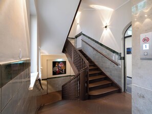 A modern staircase with a wooden handrail and a glass railing, leading to an elevator. - Smart Stay Hotel Station Munchen (Munich)